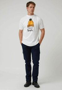 Camiseta blanca de algodón con un gráfico de un gorro de punto amarillo con un pom-pom verde y el texto "Altonadock company Winter."