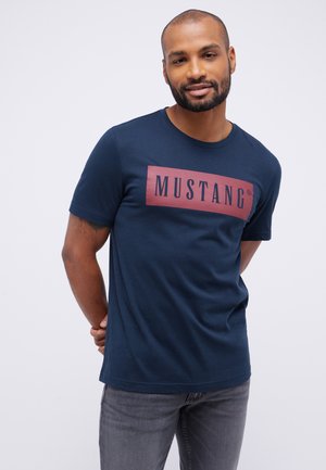 Námořnická modrá bavlněná tričko s velkým červeným obdélníkovým logem "MUSTANG". Krátké rukávy a kulatý výstřih. Jednoduchý, ležérní střih.