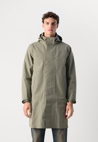 Gabardina larga, impermeable, de color verde oliva claro, con capucha, cierre a presión y bolsillos laterales. Textura suave con costuras ocultas.