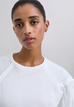 White cotton sweatshirt with raglan sleeves and puffed accents. Features a round neckline and a smooth, soft texture.