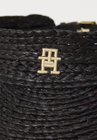 Svart vävd halm väska med en guldtrådsbroderad logotyp. Texturerad yta med rundad toppkant och platt botten.