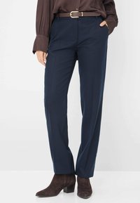 Navyblauwe op maat gemaakte broeken met een gladde textuur, voorzien van een bruine riem en een nauwsluitende pasvorm, gecombineerd met donkerbruine enkellaarzen.
