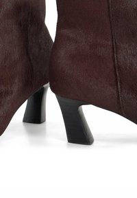Burgundy ankle boots made of soft, textured material with a curved, block heel and clean stitching along the seams.