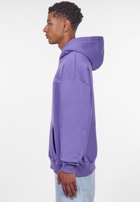 Lilla hoodie lavet af blødt stof. Har en stor hætte, oversized pasform, forlomme og ribbestrikkede manchetter. Minimalistisk design uden mønstre.