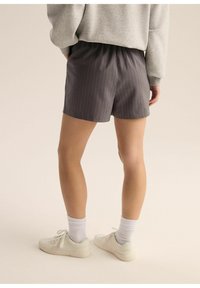 Szare szorty w prążki z elastycznym paskiem, widok z tyłu. Połączone z białymi sneakersami i skarpetkami do kostki. Gładka tekstura materiału.