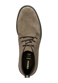 Zapato de ante gris con punta redonda, diseño de cordones, suela de goma negra y detalles en oro en la plantilla. La textura es suave y mate.