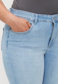 Jeans de mezclilla azul claro con un corte ajustado, que cuentan con un bolsillo frontal y cierre de cremallera, con detalles de costura sutiles alrededor de la cintura.