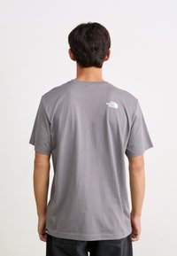 Szara koszulka z krótkim rękawem wykonana z bawełny, z okrągłym dekoltem i małym białym logo na górze pleców. Swobodny, luźny krój.