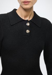 Black knit top with a collared neckline, featuring three large round buttons, textured fabric, and a fitted design.