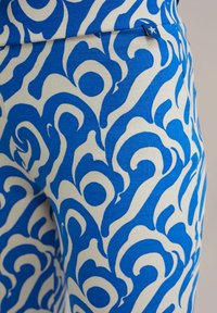 Cieši pieguļoši legingi ar zilu un baltiem viļņošanās rakstiem, izgatavoti no elastīga auduma ar ribotu tekstūru un mazu birkas detaļu.