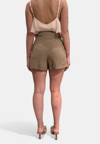 Pantaloni corti beige a vita alta con orlo ripiegato, abbinati a un top senza maniche rosa chiaro e sandali trasparenti con tacco.