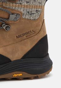 Hnedé nepremokavé turistické topánky s textúrovanou kožou a čiernymi akcentmi; obsahujú čierno-biele šnúrky a Vibram gumenú podrážku.