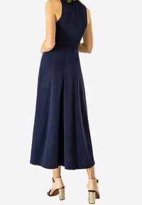 Tmavě modré šaty bez rukávů s upevněným trupem a rozšířenou sukní. Nosit s světlými lodičkami na vysokém podpatku s tlustými podpatky.