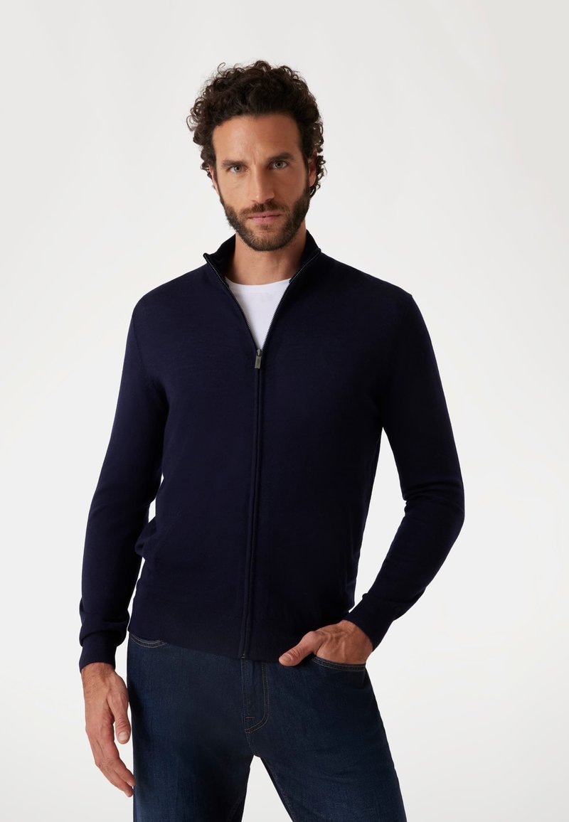 Maglione zip-up blu navy con colletto alto, maniche lunghe e texture liscia. Presenta un dettaglio con zip argentata e un design aderente.