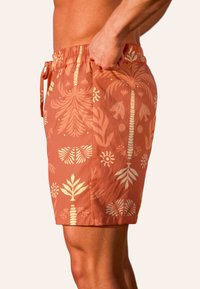 Herren-Schwimmshorts in rosé-orange mit weißen Palm- und Blumenmustern, ausgestattet mit einem elastischen Bund und Seitentaschen. Hergestellt aus leichtem Stoff.