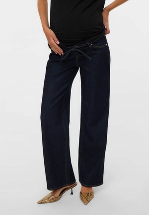 Donkerblauwe denim broek met wijde pijpen, een trekkoord in de taille en gele stiksels. Gepaarde met slangenpatroon hoge hakken.
