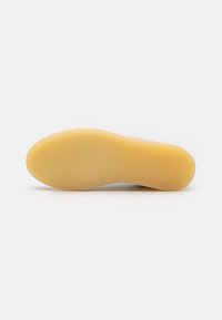 Sko såle med et glatt, lyst brunt gummimateriale med fiskebensmønster og flat design, som viser logoavtrykk og teksturdetaljer.