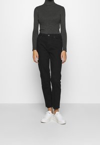 Pantalones de mezclilla negros con corte recto, combinados con un suéter de cuello alto de canalé gris oscuro y zapatillas blancas. Diseño sencillo, estilo minimalista.