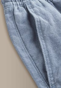 Gros plan sur un pantalon en tissu texturé bleu clair avec des coutures visibles et une ceinture élastique.