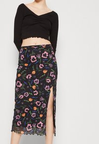 Černý dlouhý rukáv crop top s výstřihem do V a volánkovým lemem; průhledná midi sukně s barevným květinovým vzorem a bočním rozparkem.