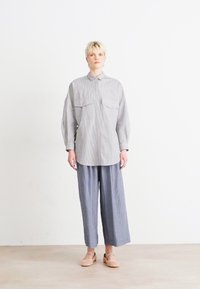 Camicia a righe con due tasche sul petto, abbinata a pantaloni larghi a righe. Tessuto leggero, grigio chiaro e blu. Scarpe flat completano l'outfit.