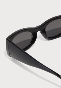 Occhiali da sole neri con un design audace e angolare. Presentano lenti scure e una finitura in plastica lucida e liscia. Sponde affusolate.