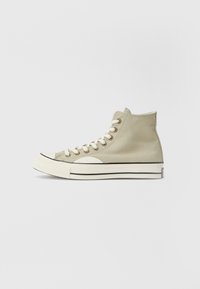 Hochschnittige Leinensneaker in Hellbeige mit weißen Schnürsenkeln, schwarzem Besatz und Gummikappe. Verfügt über einen strukturierten Stoff und runde Ösen.