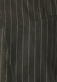 Svart tyg med vita vertikala smalrandiga ränder, med en texturerad väv och en fickdetalj till höger.
