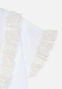 Top de algodón blanco con mangas de encaje con volantes que presentan patrones florales y pequeños detalles de corte. Textura suave en general.