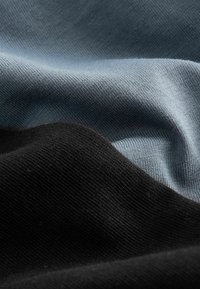 Baumwollstoff in Schwarz- und Blautönen, mit einer glatten Textur und subtilem Rippenmuster. Der Stoff fällt sanft und bildet weiche Falten.