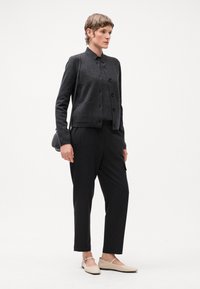 Cárdigan negro de botones, top gris y pantalones de rayas, combinados con unas bailarinas beige. Los accesorios incluyen un pequeño bolso cruzado negro.