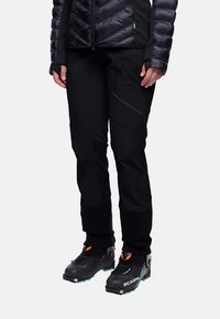 Zwarte outdoorbroek met een aansluitend ontwerp, voorzien van een gestructureerde stof en zijzakken. Gecombineerd met zwarte laarzen met kleurrijke accenten.