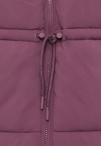 Gewatteerde vest in donker mauve met een volledige rits, verstelbare trekkoord taille en een zachte textuur. Beschikt over drukknoopjes op de taille.