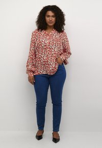 Blusa de estampado rojo y blanco con mangas largas, combinada con jeans ajustados azules y bailarinas de punta negra.