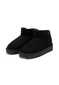 Botas de tobillo de ante negro con punteras redondeadas, textura suave y suela de goma plana. Presentan un puño corto y doblado alrededor del tobillo.