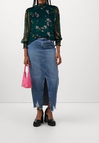 Zielona kwiecista bluzka z przezroczystymi rękawami, niebieska spódnica jeansowa z przednim rozcięciem, różowa torebka i czarne platformy na obcasie.