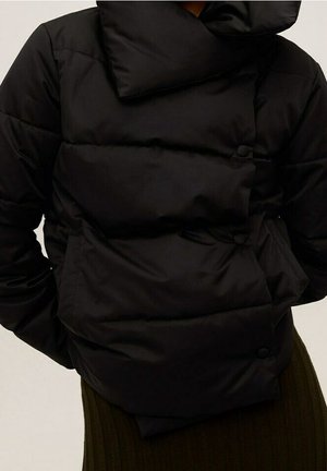 Doudoune noire avec col montant et fermeture asymétrique à boutons, portée sur une jupe ou un pantalon côtelé foncé.