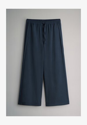 Pantalones de pierna ancha en azul oscuro con cintura elástica y cordón, con bolsillos laterales, mostrados sobre un fondo gris claro.