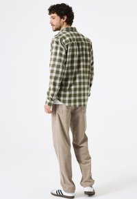 Camisa de cuadros verde y crema con botones, de manga larga, en tela de algodón, con un ajuste holgado, combinada con pantalones de pana beige y zapatillas con acentos negros.