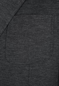 Tela gris oscuro con una textura sutil; presenta un bolsillo parche con costuras cuidadas, integrado en el diseño de una prenda.