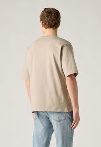 Μπεζ βαμβακερό μπλουζάκι με κοντά μανίκια, στρογγυλή λαιμόκοψη και άνετη εφαρμογή. Φορεμένο με ανοιχτόχρωμο μπλε τζιν παντελόνι, που δείχνει έναν απλό σχεδιασμό.