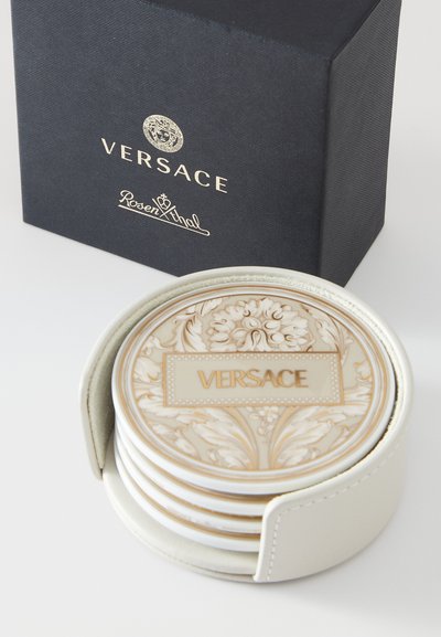 Podtácky Versace v bílém držáku, zdobené složitými zlatými a krémovými květinovými vzory. Představují se v černé značkové krabičce se zlatými akcenty.