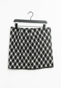 Falda mini de cuadros en blanco y negro con material de lana texturizada, que presenta un patrón de diamantes y un dobladillo recto. Colgada de una percha negra.