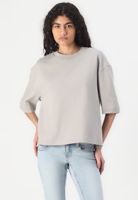 Lys grå t-skjorte med kort erm og rund hals, i en avslappet passform, laget av myk, teksturert stoff, kombinert med blå jeans.