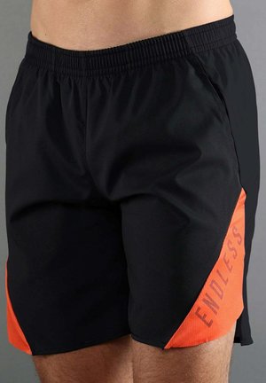Pantalones cortos deportivos negros con paneles naranjas en los lados, con la palabra "ENDLESS" en letras mayúsculas en el panel derecho.