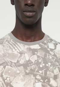 Κοντομάνικο T-shirt από βαμβάκι σε ανοιχτό γκρι, με σχέδιο που απεικονίζει διάφορες υφές, σχήματα και λεπτομέρειες· λαιμός με ριμπ ύφανση.