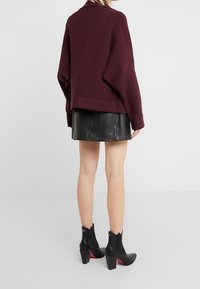 Burgundy oversized stickad tröja, texturerat tyg, sänkt axel, parat med en svart läder mini kjol och svarta klackade ankelstövlar.