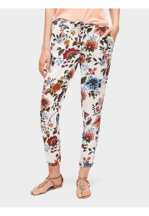 Białe, dopasowane spodnie z czerwonym, niebieskim i pomarańczowym motywem kwiatowym, z talią na sznurek i bocznymi kieszeniami, noszone z jasnobrązowymi sandałami.