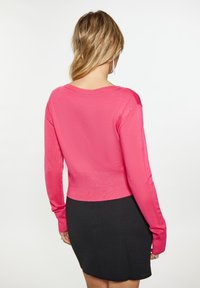 Maglione rosa aderente a maglia con maniche lunghe e scollatura a barca, abbinato a una gonna nera. Texture liscia, design semplice, senza motivi visibili.