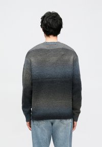 Pulover iz temnosive do svetlo modre barvnega prehoda, pleten z rebrastim robom in okroglim ovratnikom, kombiniran s svetlo modrimi kavbojkami.